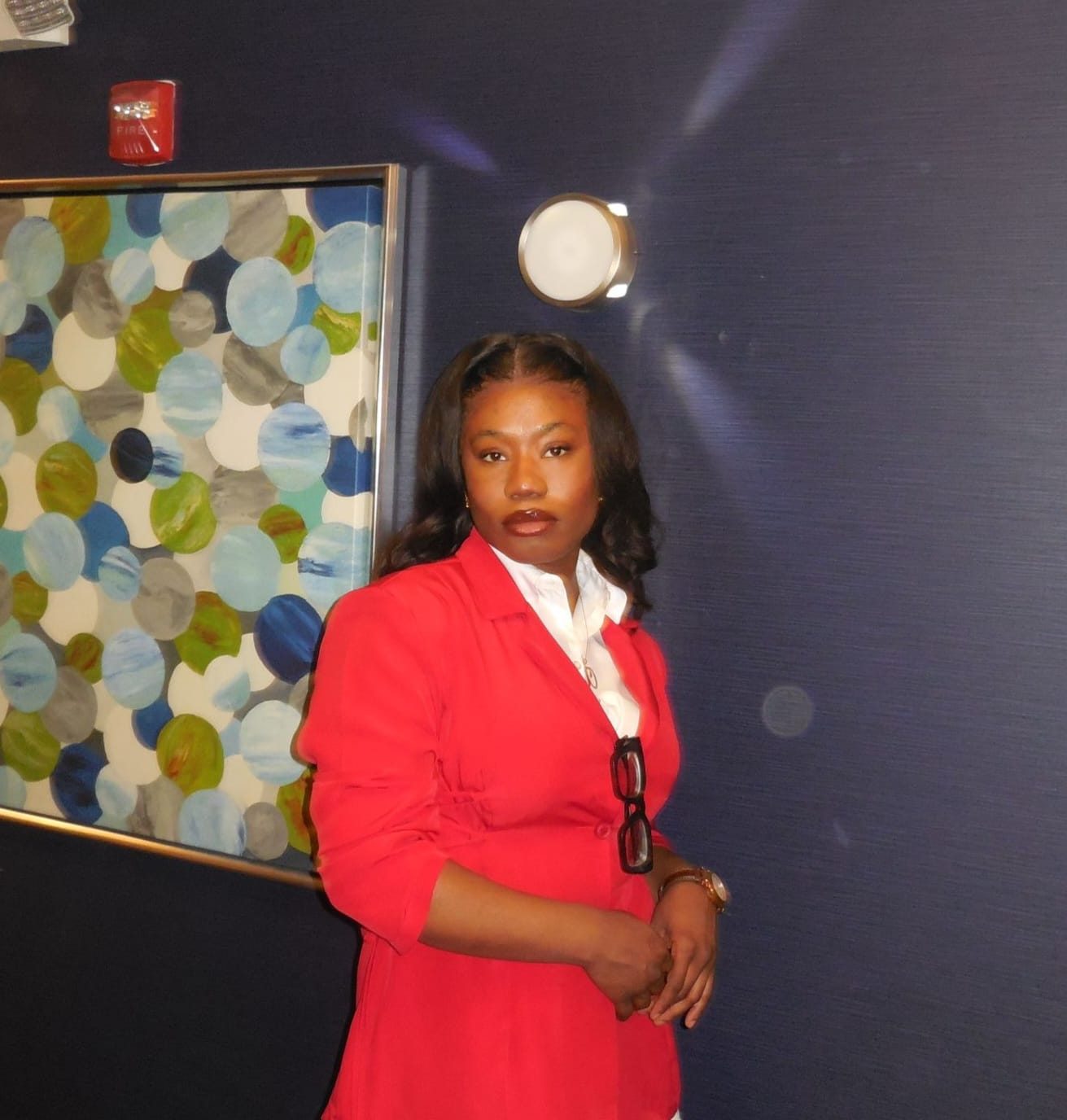 Phoebe Oyimi in a red jacket, standing by a painting
