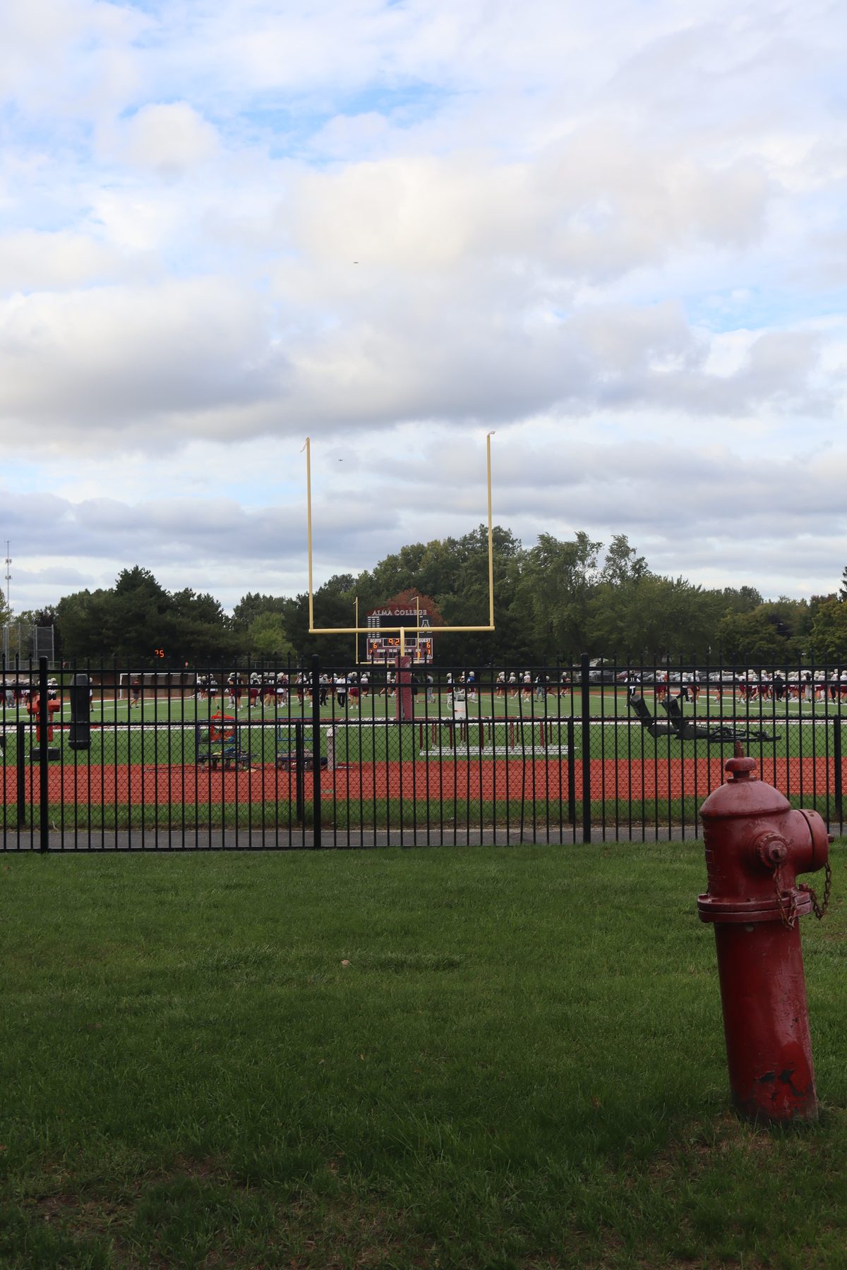 A football field behind a black fence, a red hydrant in the grass