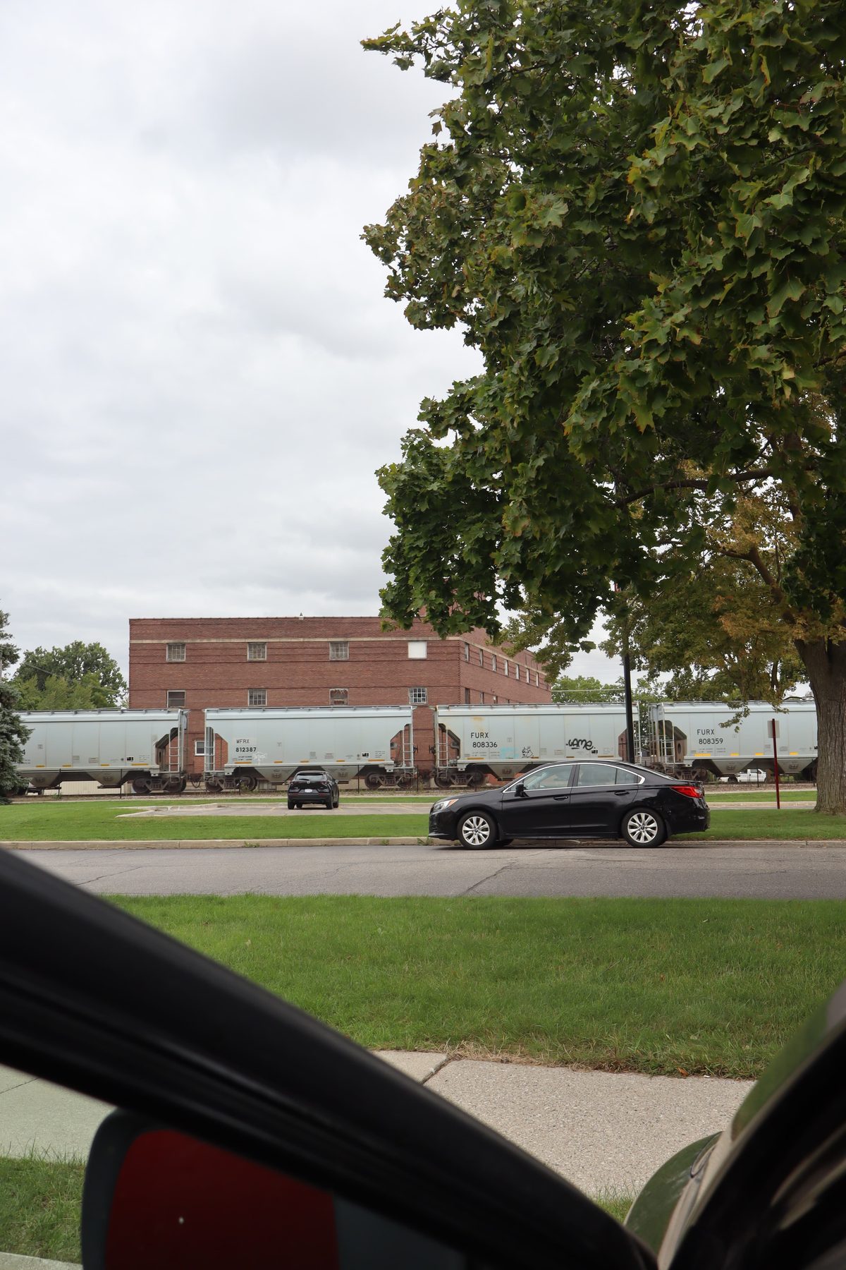 Grain cars on a railway line, seen past a parked car